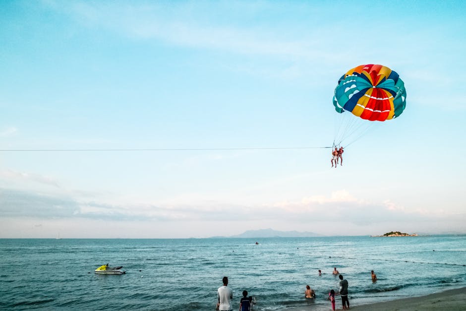 Exciting parasailing experience over the ocean with a vibrant parachute and scenic beach view.